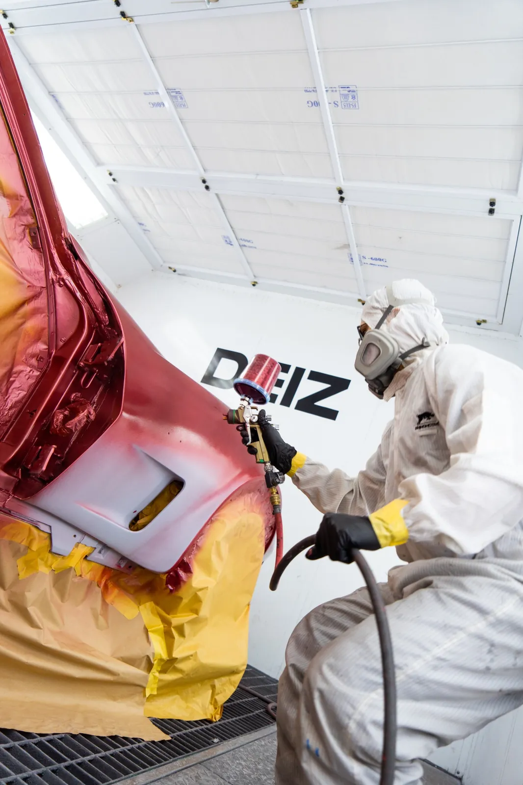 DEIZ Garage technician applying paint to a vehicle inside the paint booth